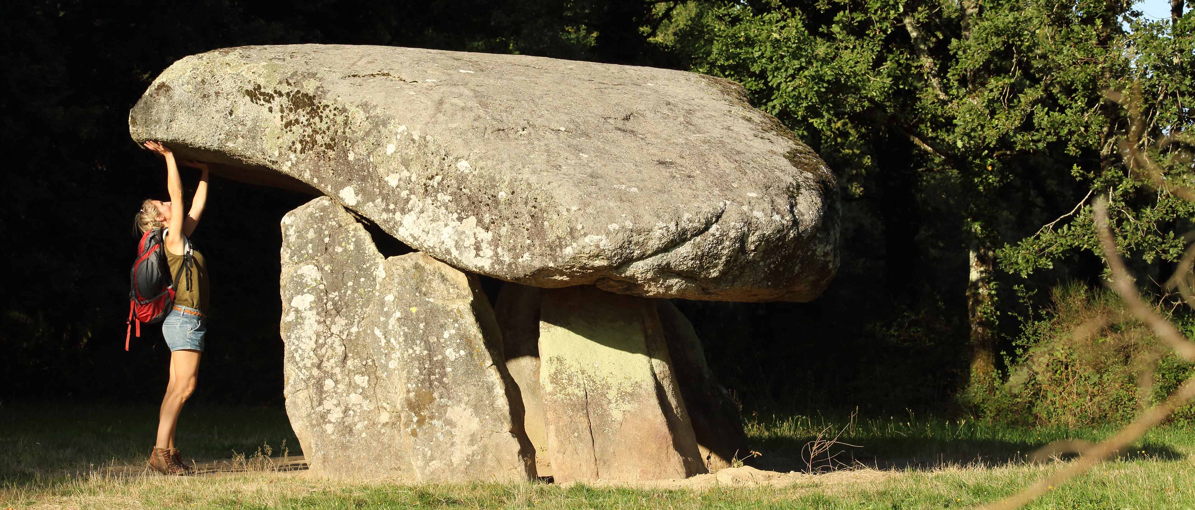 Randonneuse soulevant un dolmen dans une clairière