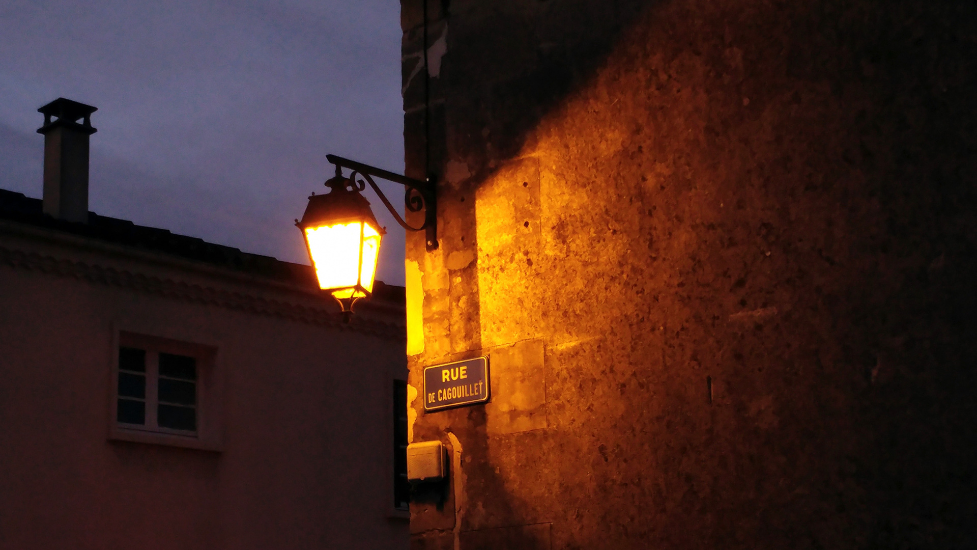 Un réverbère éclaire un vieux mur de Cognac dans des teintes caramel et orangées.